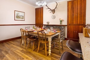 A dining room with a wooden table set for four, surrounded by chairs, a stone fireplace, and a mounted deer head.