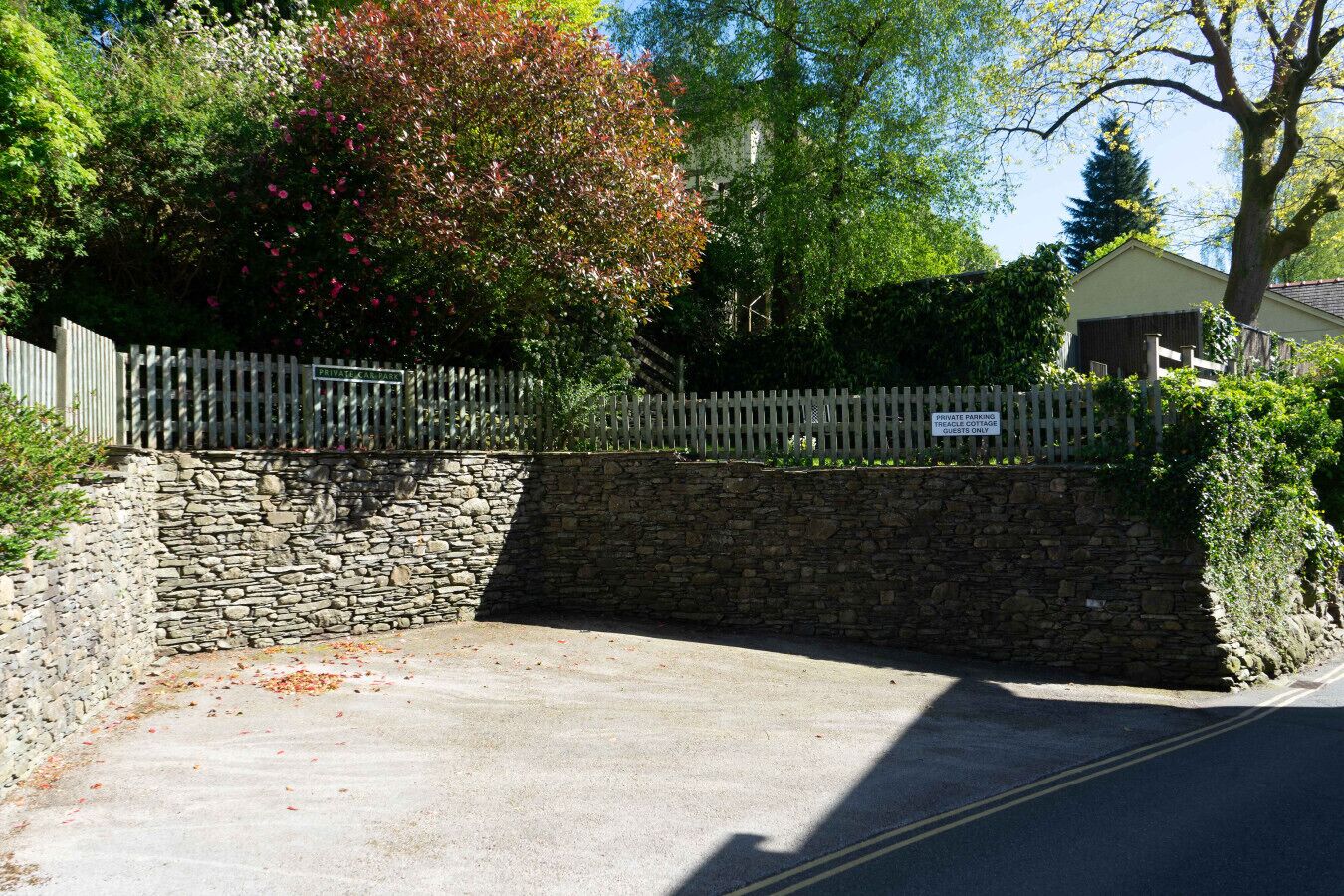 A private parking area with a stone wall and a wooden fence, leading to a building with a sign indicating it's for guests only.