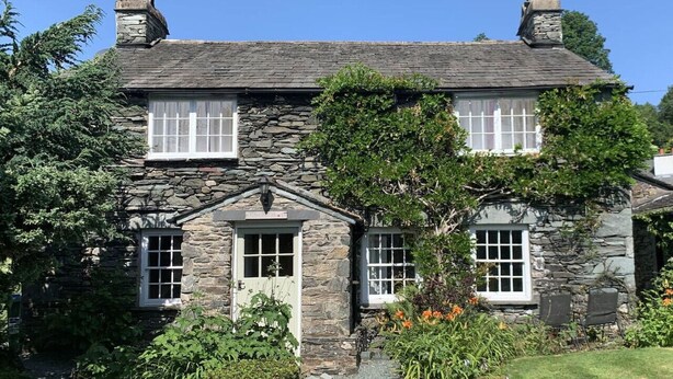 A stone house with a gabled roof, two chimneys, and a small porch.