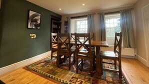 A dining area with a wooden table and chairs, a patterned rug, and a bookshelf.