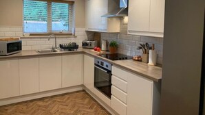 A modern kitchen with white cabinetry, a built-in oven, a microwave, and a window with blinds.