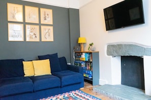 A living room with a blue sofa, a bookshelf, a fireplace, and framed botanical prints on the wall.