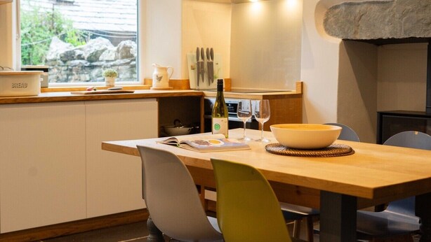 A compact kitchen with a window, a dining table, chairs, and a stone accent wall. - Holmdale - Central Ambleside (Ambleside)