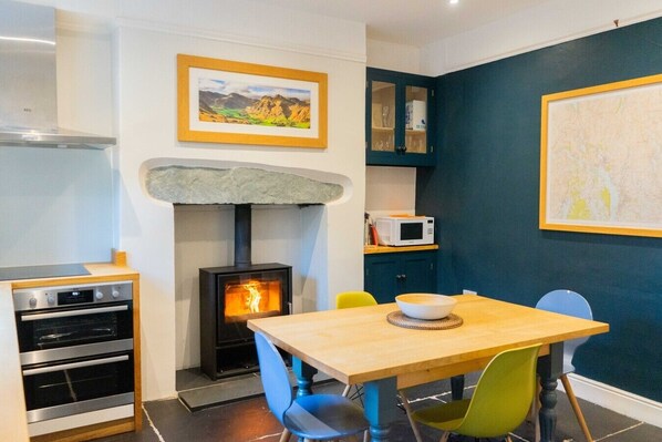 A compact kitchen with a wood-burning stove, a microwave, and a dining area with chairs.