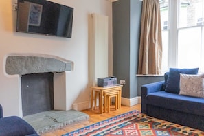 A living room with a stone fireplace, a television mounted on the wall, a blue sofa, and a patterned rug.