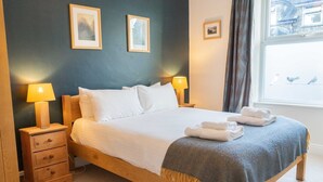 A neatly made bed with white linens, two bedside lamps, a small wooden nightstand, and a window with a view of birds. - Holmdale - Central Ambleside (Ambleside)