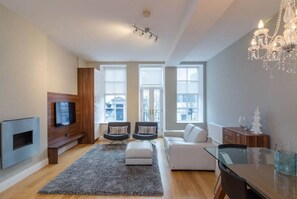A modern living room with a flat-screen TV, two armchairs, a sofa, a glass coffee table, and a chandelier. - Smithfield Apt in Belfast's Cathedral Quarter (Belfast)