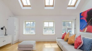 A bright room with skylights, a sofa with colorful cushions, and a white cabinet.