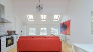 A modern kitchen with a red sofa, skylights, and a city view.
