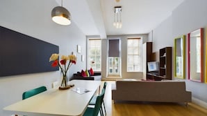 A modern living space with a dining area, a sofa, and a TV in the background.