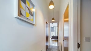 A narrow hallway with a carpeted floor, a pendant light, and a framed abstract artwork on the wall.