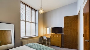 A bedroom with a bed, a desk with a chair, a television, and a wardrobe.