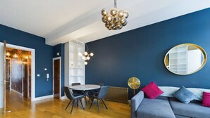 Uma sala de estar moderna com uma parede azul, um sofá cinza com almofadas rosa e azul, um espelho redondo e um candelabro.