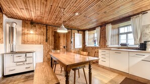 Una habitación con paneles de madera, una mesa de comedor de madera, armarios blancos y una ventana con cortinas.