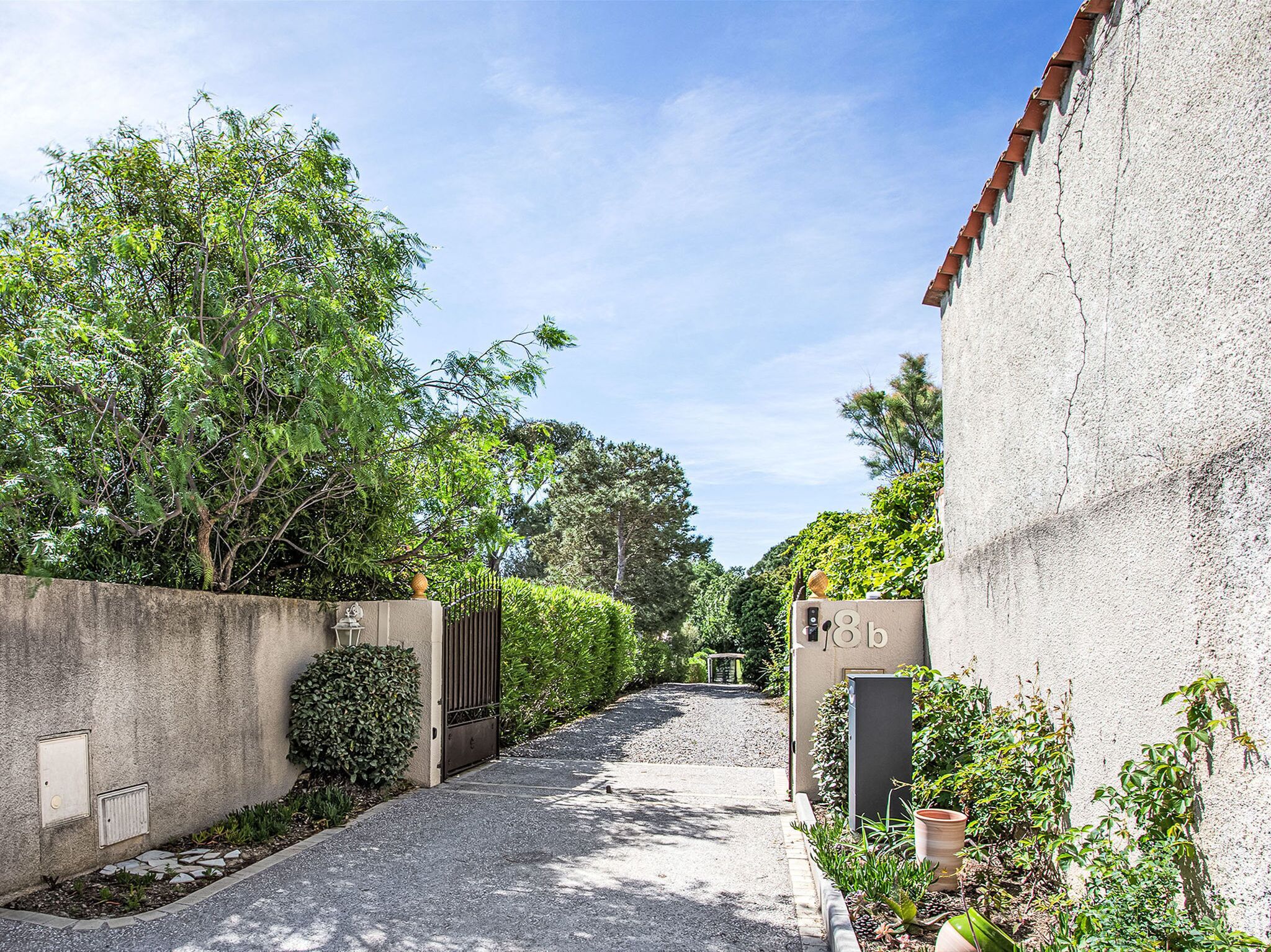 A narrow pathway leading to a gated entrance with a concrete wall on one side and a building on the other.