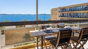 A balcony with a table set for dining, overlooking a body of water and a building. - Le Grand Large by Interhome (Sainte Maxime)