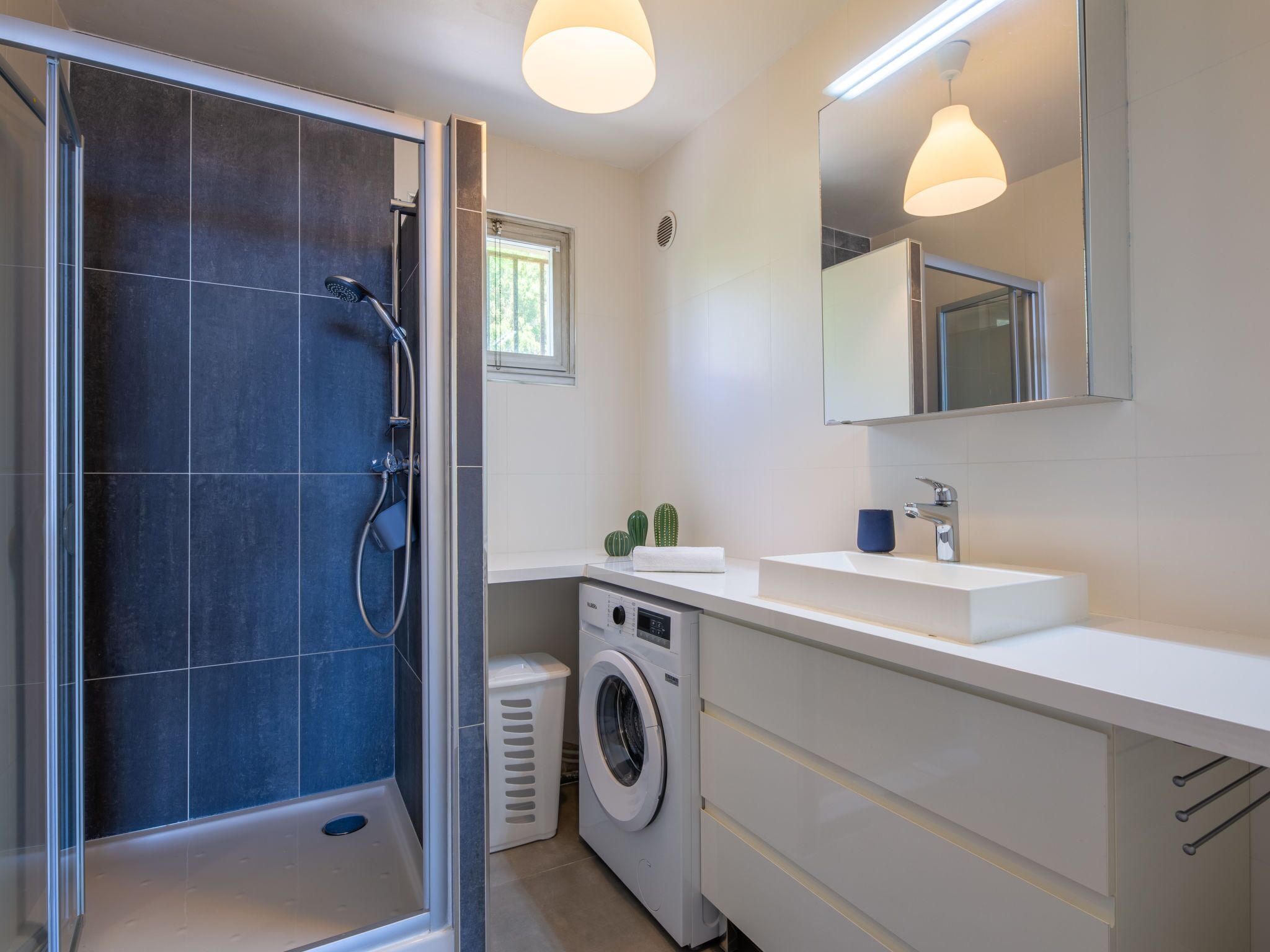 Une salle de bain moderne dotée d’une douche à parois de verre, d’un lave-linge encastré et d’un grand miroir au-dessus du lavabo.