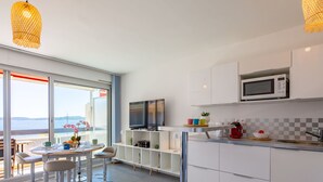 A modern kitchen with a large island, white cabinets, and a view of the sea through the sliding glass doors. - Le Grand Large by Interhome (Sainte Maxime)