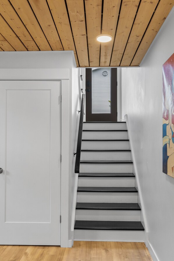 A staircase with white walls, a wooden ceiling, and a door on the left. - Brighton Charlottetown 4BR Home – Spacious, Family-Friendly, Private Yard (Charlottetown)
