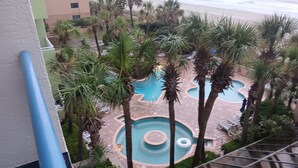 A rooftop pool area with multiple circular pools surrounded by palm trees and lounge chairs.