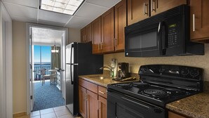 A modern kitchen with wooden cabinets, a black microwave, a stove, and a refrigerator.