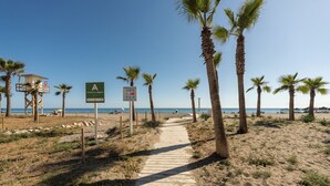 Ein Strandweg mit Palmen, einem Rettungsturm und Strandschildern.