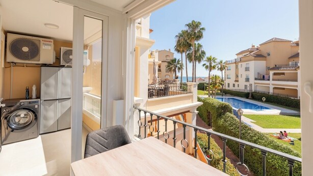 Ein Balkon mit Waschmaschine, Tisch und Blick auf Pool und Palmen.