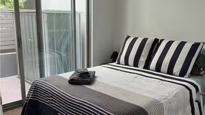 A bedroom with a bed, striped bedding, a pillow, and a view through a sliding glass door.