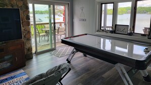 A pool table in a room with a stone wall, a television, and a view of a lake.