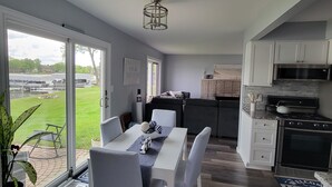 A modern kitchen with white cabinets, a stainless steel oven, and a dining area with a white table and striped chairs.