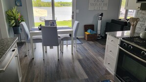 A modern kitchen with a large window overlooking a lake, a dining area with chairs, and a kitchen counter.