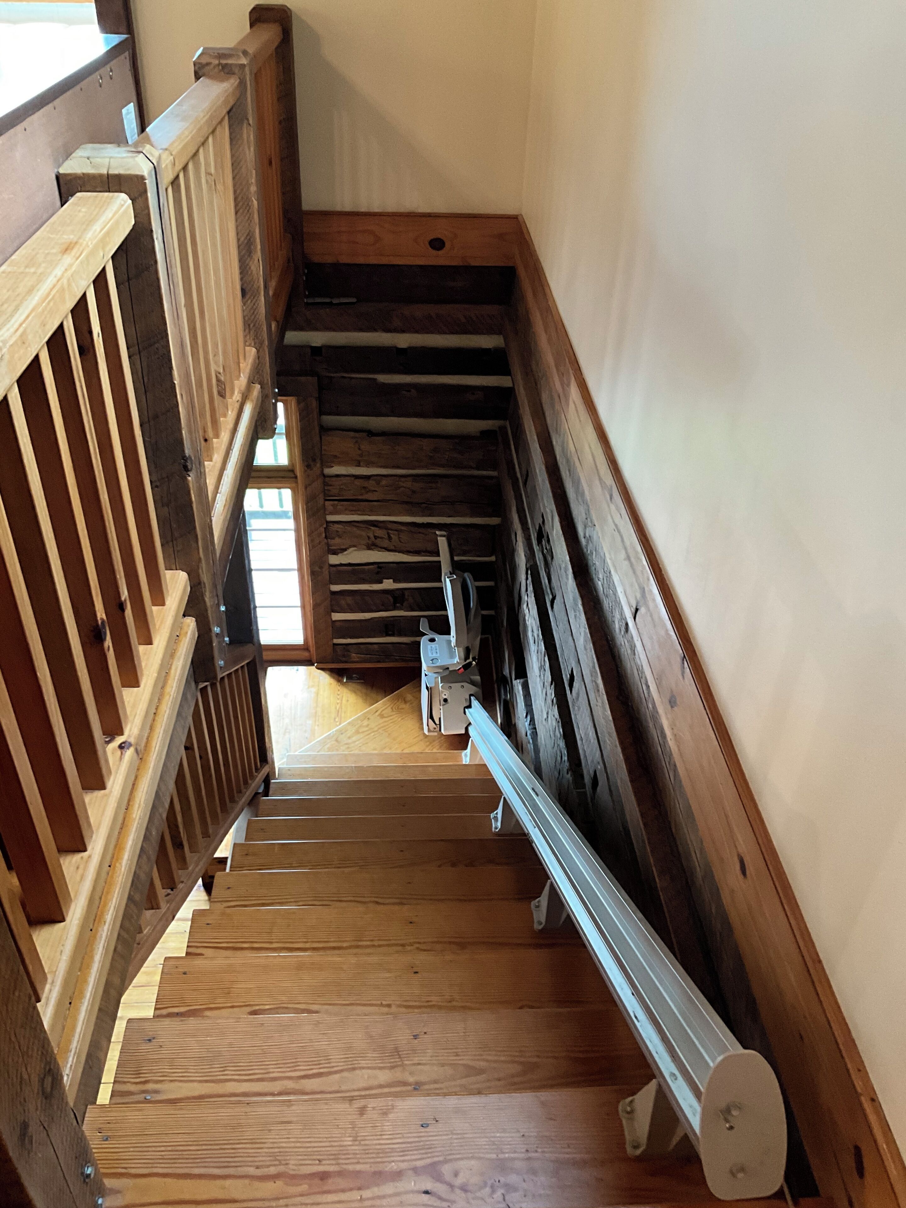 Una escalera de madera con barandilla, peldaños de madera y una barandilla metálica a la derecha.