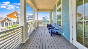 A covered porch with wooden flooring and white railings, featuring several blue Adirondack chairs. - Elegant Beach House with views, resort pool, golf, restaurants - steps to beach (Port Aransas)
