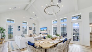 A spacious living room with a large dining table, wicker furniture, and a chandelier. - Elegant Beach House with views, resort pool, golf, restaurants - steps to beach (Port Aransas)