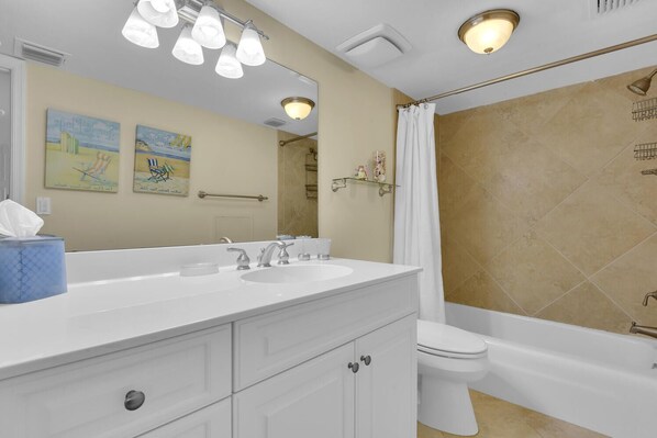 A bathroom with a white vanity, two sinks, a toilet, and a shower area.