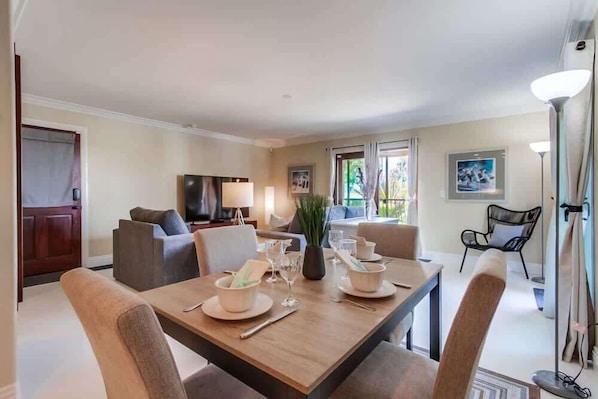 A dining area with a table set for four, a sofa, a TV, and a chair.