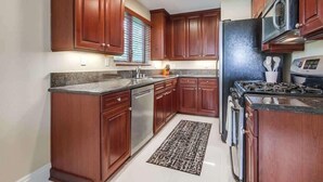 Une cuisine avec des meubles en bois, des appareils électroménagers en acier inoxydable et un tapis à motifs.
