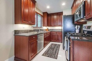 A kitchen with wooden cabinets, stainless steel appliances, and a patterned rug.