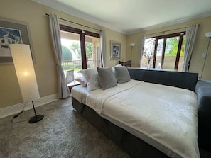 A bedroom with a bed, curtains, a lamp, and a view of the outdoors.