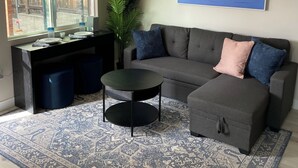A living room with a grey sofa, a coffee table, a patterned rug, a painting of boats, and a window with a view of a wooden fence. - 1br/1ba newly renovated, newly furnished downstairs unit of a duplex (San Diego)