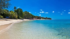 A beach with clear turquoise water, a sandy shore, and a line of trees and umbrellas in the background. - Villa with Private Pool and Sandy Lane Beach Club Access - Coral Gables (Sandy Lane)