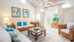 A living room with a sofa, a coffee table, and a wicker chair. There is a door leading to a balcony with chairs. - Villa with Private Pool and Sandy Lane Beach Club Access - Coral Gables (Sandy Lane)