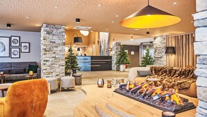 A modern lobby with a stone accent wall, a reception desk, a fireplace, and a seating area with a sofa and chairs. - Odalys Collection Le Mont d'Auron by Interhome (Auron)
