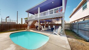 A two-story house with a covered patio area, a swimming pool, and a fenced backyard. - Private Heated Pool, Pet Friendly, Fire Pit (Port Aransas)