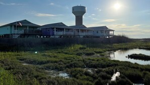A waterfront property with multiple houses, a water tower, and a marshy foreground. - Private Heated Pool, Pet Friendly, Fire Pit (Port Aransas)