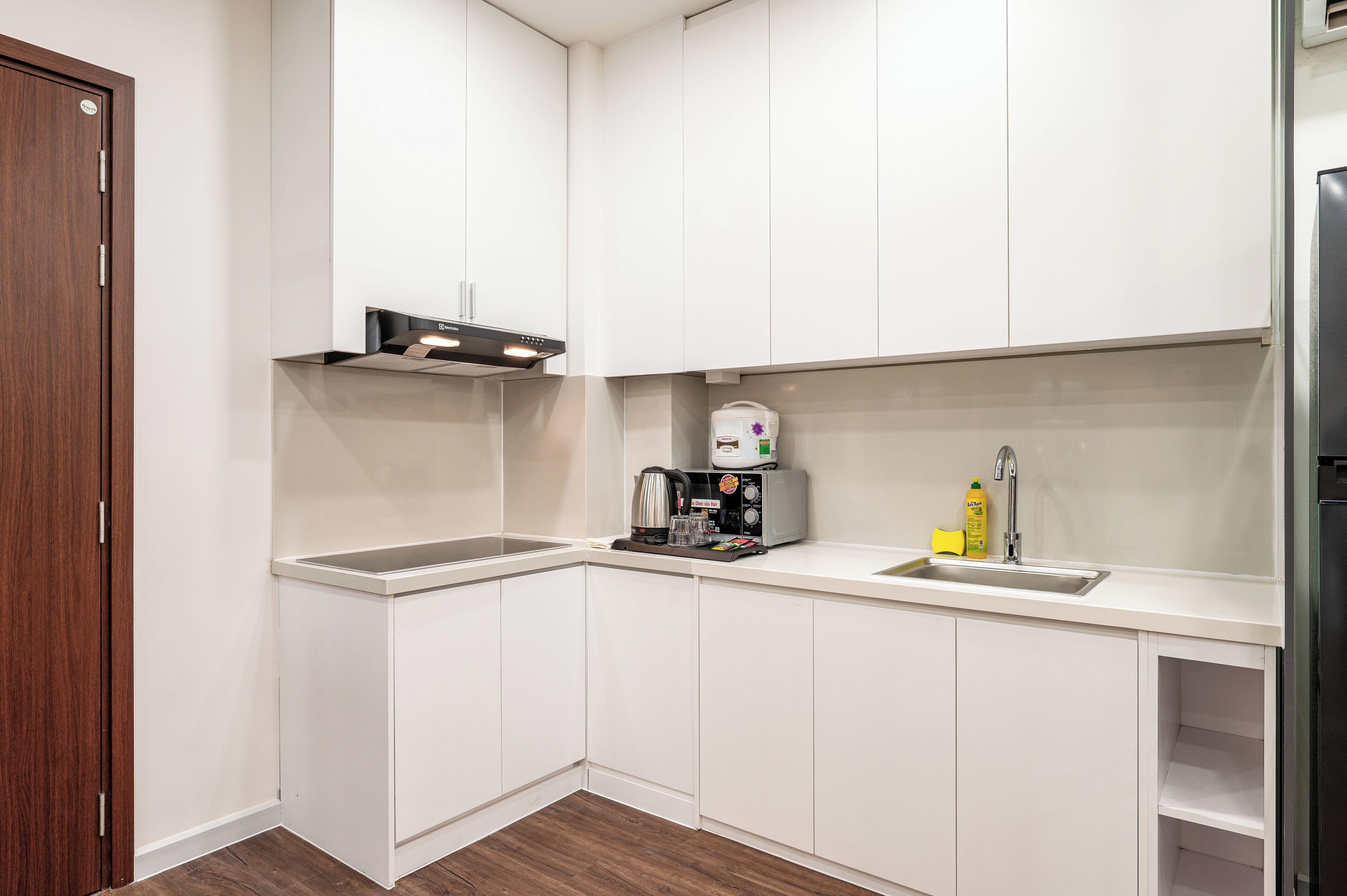 Eine kleine Küche mit weißen Schränken, einer integrierten Kaffeemaschine, einem Spülbecken und einem Kühlschrank.