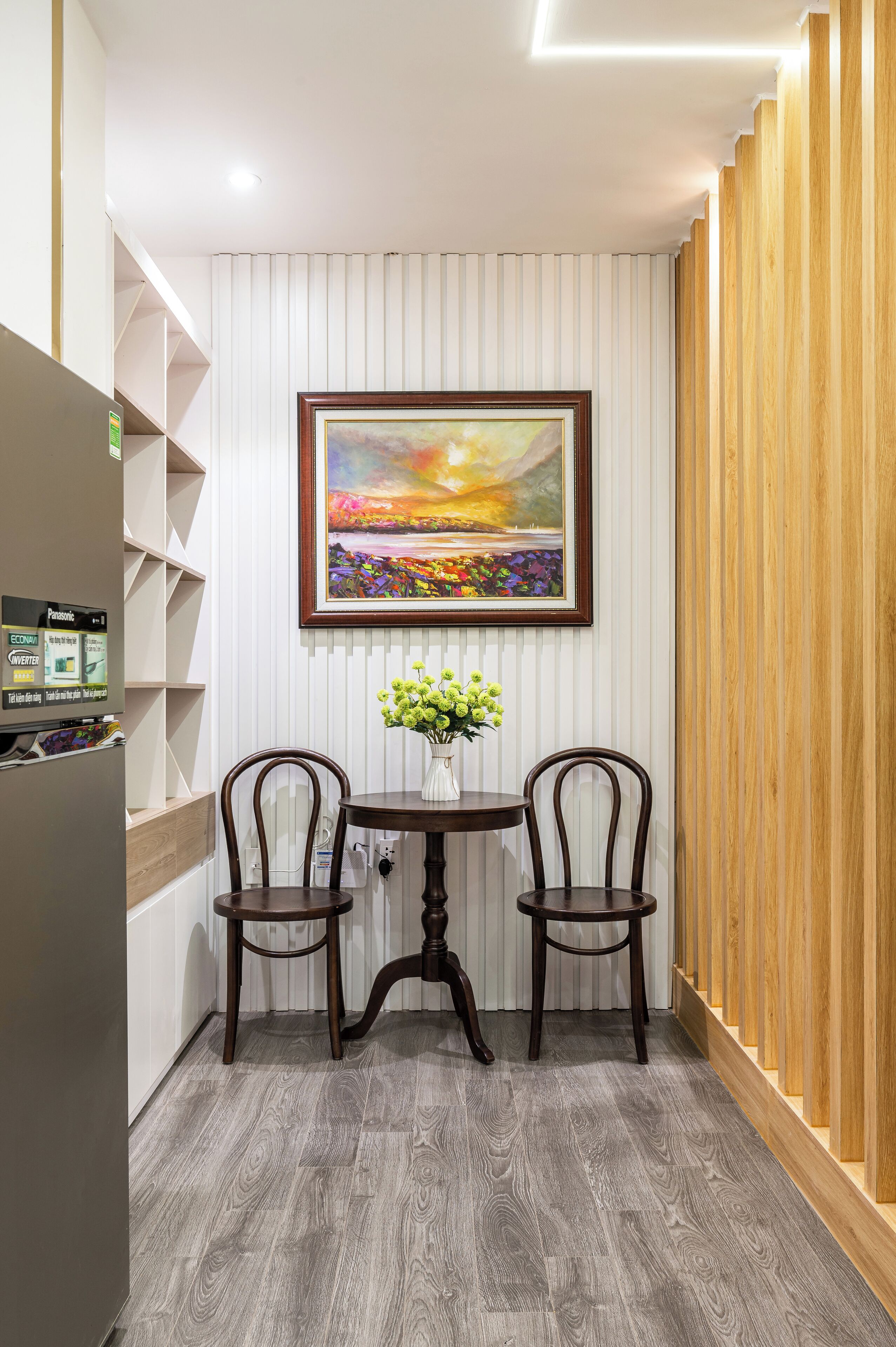 A modern kitchen with a built-in refrigerator, wooden cabinets, and a dining area with two chairs and a table.