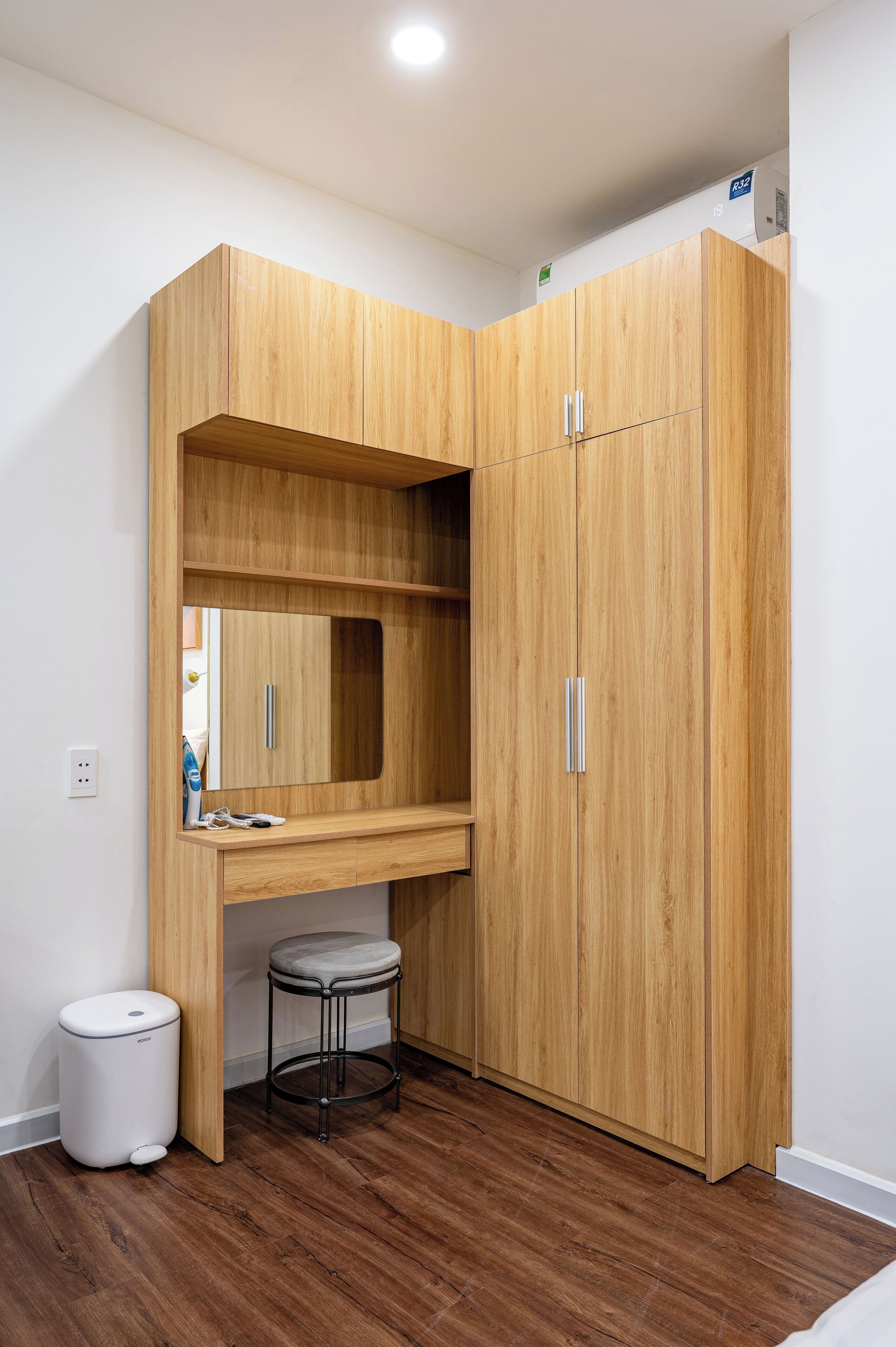 Ein kleines Zimmer mit einem Holzschrank, einem kleinen Hocker und einem Mülleimer.