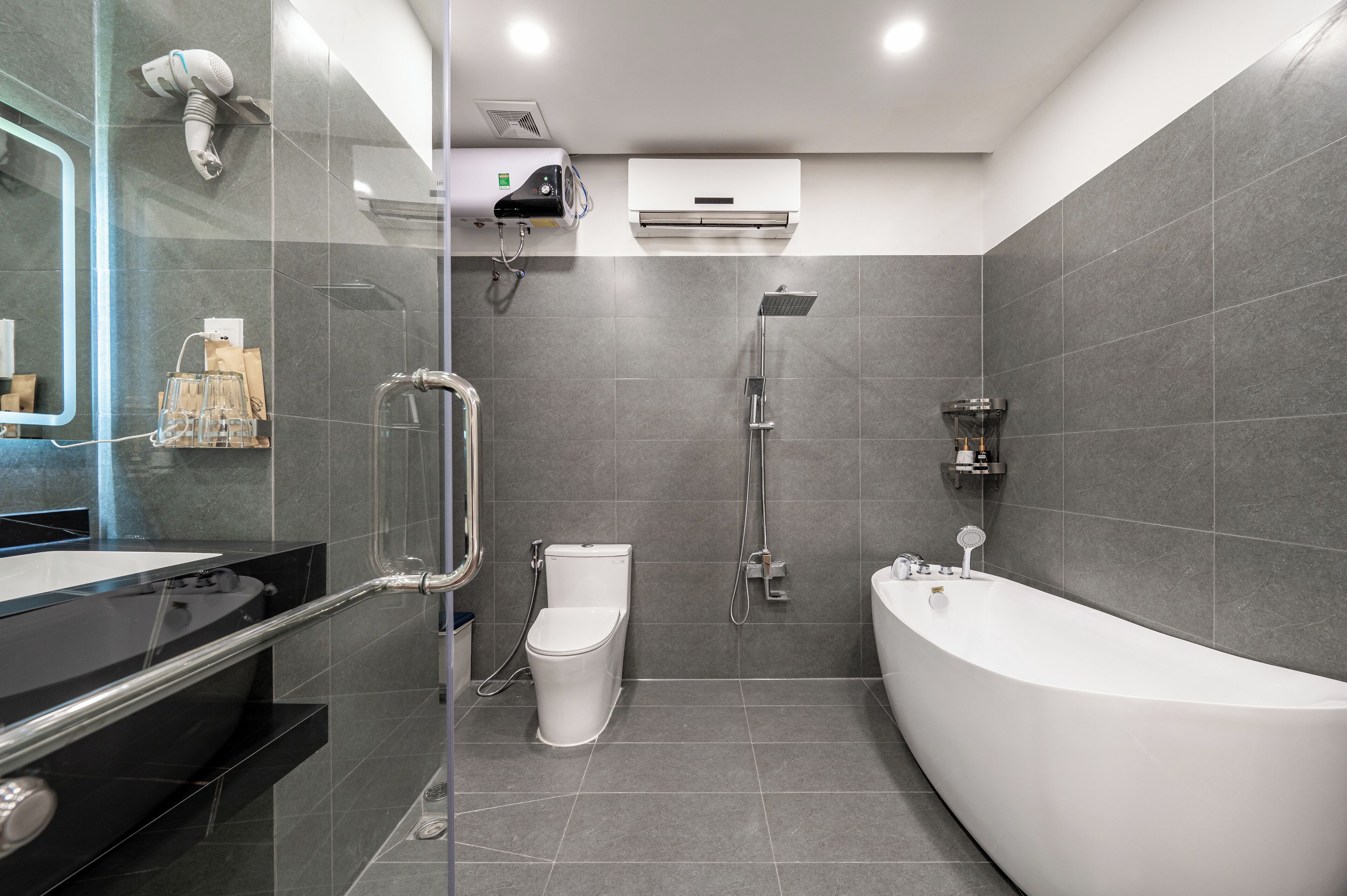 Un baño moderno con cabina de ducha de vidrio, inodoro independiente, bañera y tocador con espejo.