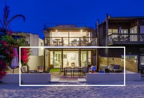 A modern two-story house with a balcony, outdoor seating area, and a barbecue setup.